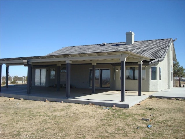 back of property with a patio, a tile roof, a chimney, and stucco siding