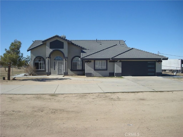 view of front facade with stucco siding, a tile roof, concrete driveway, and an attached garage