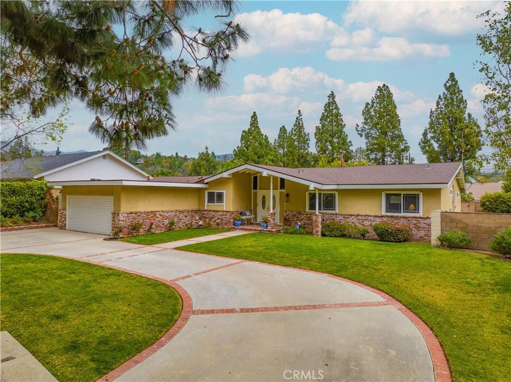 ranch-style house with concrete driveway, stucco siding, fence, an attached garage, and a front lawn