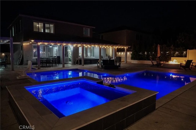 pool at night featuring an outdoor pool, a patio, outdoor dining area, an in ground hot tub, and a fire pit