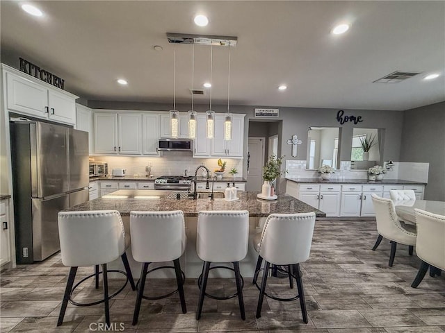 kitchen with tasteful backsplash, a sink, white cabinets, a kitchen island with sink, and appliances with stainless steel finishes