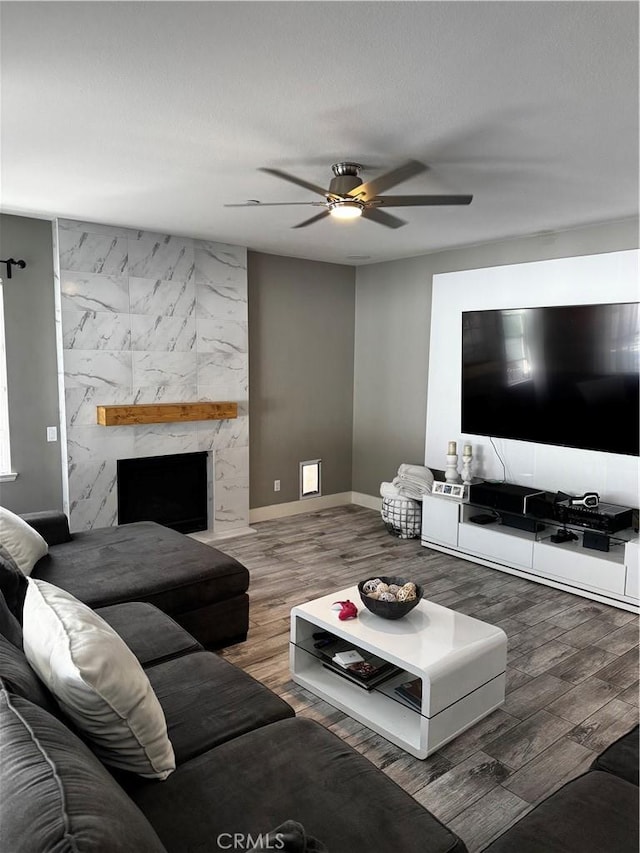 living area featuring baseboards, a premium fireplace, a ceiling fan, and wood finished floors