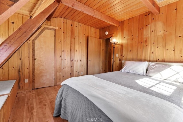 bedroom featuring wood walls, beamed ceiling, and light wood finished floors