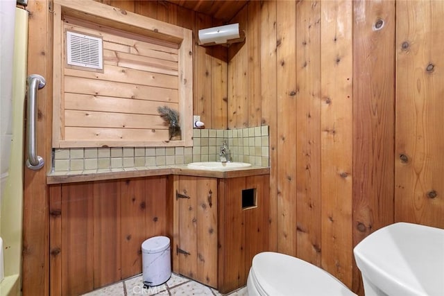 bathroom with wood walls, toilet, tile patterned floors, vanity, and tasteful backsplash