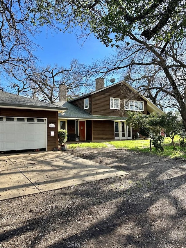 view of front facade featuring driveway, a chimney, and a garage