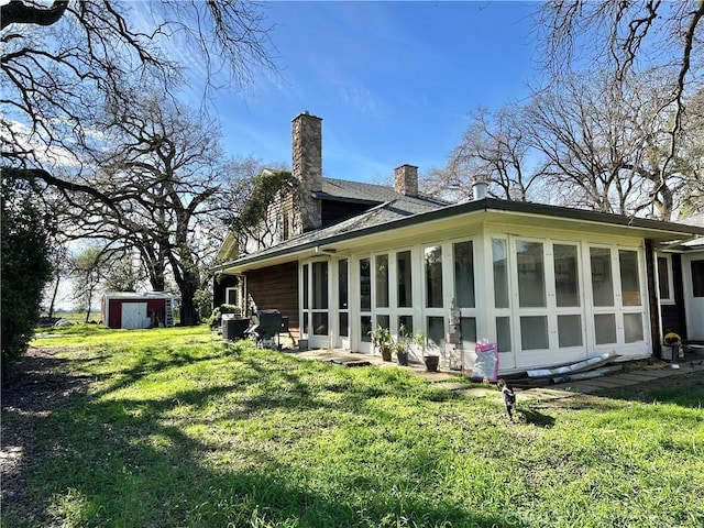 view of side of property with a sunroom, a chimney, a storage unit, an outbuilding, and a yard