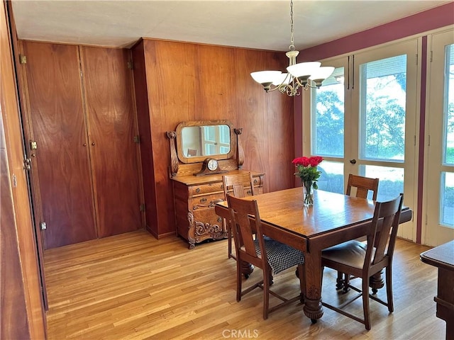dining space featuring light wood-type flooring, wood walls, and a chandelier