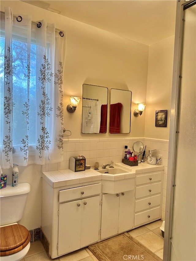 bathroom with toilet, vanity, wainscoting, tile patterned flooring, and tile walls