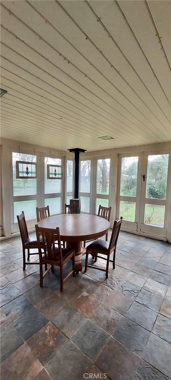 sunroom featuring a wood stove, french doors, wood ceiling, and stone tile floors