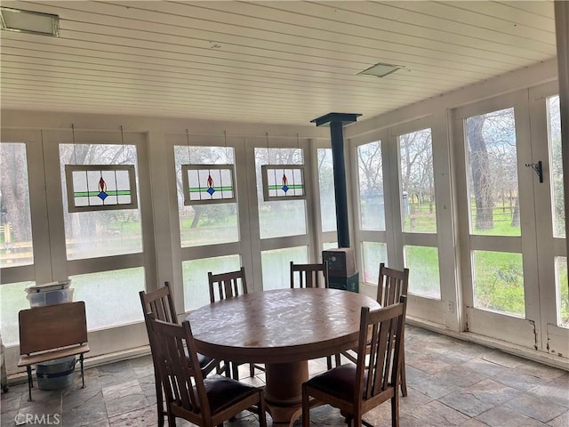 sunroom with a wood stove, wood ceiling, and stone tile floors