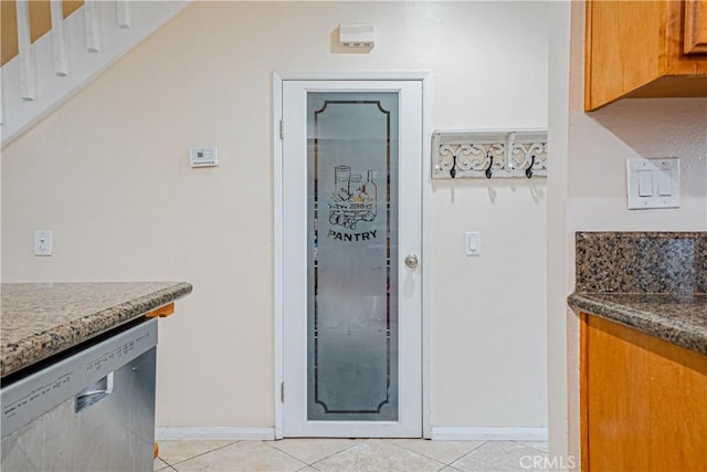 25301 Pine Creek Ln, Wilmington, CA 90744 - kitchen with stainless steel dishwasher, light tile patterned floors, baseboards, brown cabinets, and stone countertops