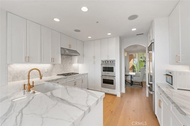 7 Suprema Dr, Newport Coast, CA 92657 - kitchen with a sink, stainless steel appliances, under cabinet range hood, arched walkways, and light wood-style floors