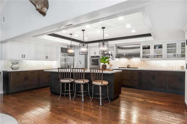 2565 Cliff Rd, Upland, CA 91784 - kitchen with stainless steel appliances, range hood, a tray ceiling, a center island with sink, and white cabinetry