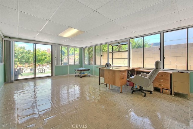 office area with a paneled ceiling, healthy amount of natural light, baseboards, and a wall of windows
