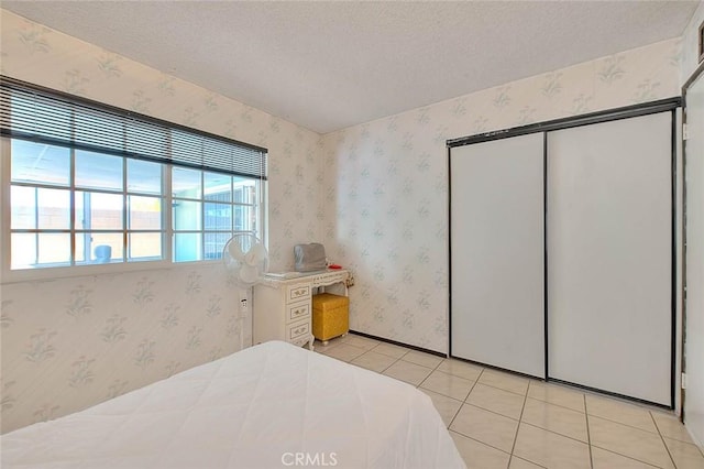 bedroom with a textured ceiling, wallpapered walls, light tile patterned flooring, and a closet