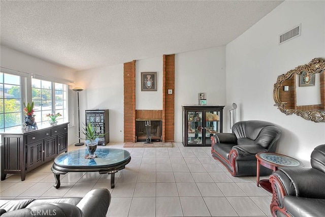 living room with a brick fireplace, a textured ceiling, light tile patterned flooring, and vaulted ceiling