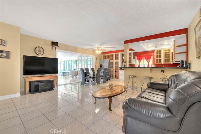 living area with light tile patterned floors, a ceiling fan, baseboards, and a textured ceiling
