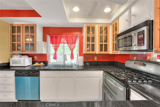 kitchen with appliances with stainless steel finishes, a sink, dark countertops, white cabinets, and ornamental molding
