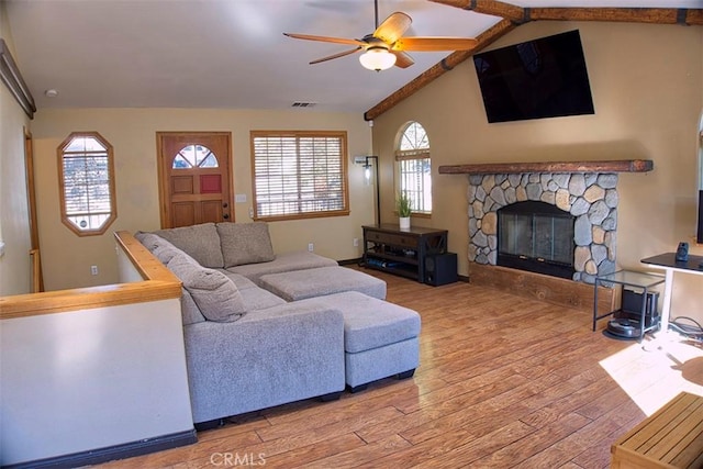 living area featuring ceiling fan, visible vents, a stone fireplace, vaulted ceiling with beams, and wood finished floors