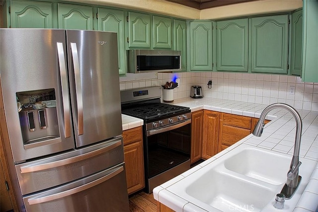 kitchen with green cabinetry, decorative backsplash, a sink, and stainless steel appliances