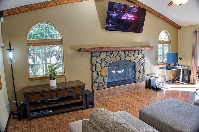 living area featuring a stone fireplace, vaulted ceiling with beams, and wood finished floors