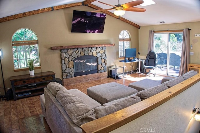 living area featuring lofted ceiling, hardwood / wood-style flooring, ceiling fan, visible vents, and a stone fireplace