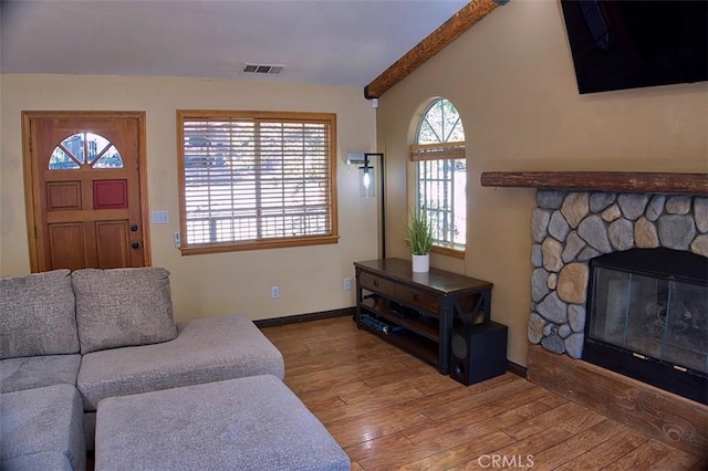 living area featuring baseboards, visible vents, a stone fireplace, vaulted ceiling with beams, and wood finished floors