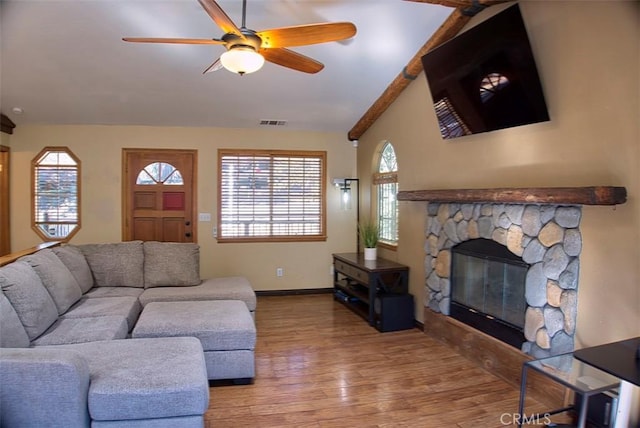 living area featuring visible vents, ceiling fan, wood finished floors, a stone fireplace, and lofted ceiling