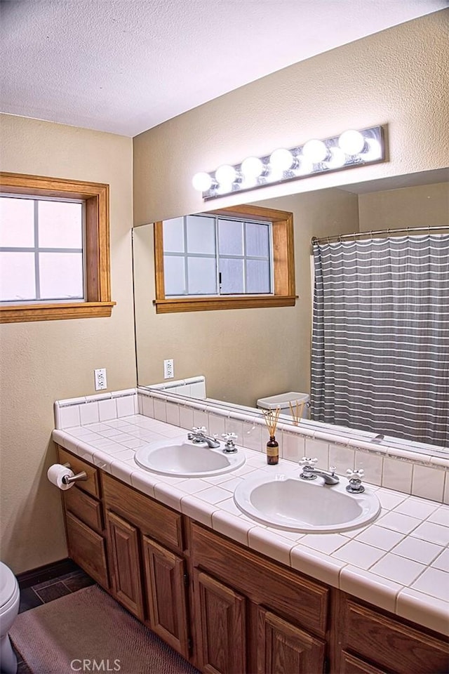 full bathroom featuring double vanity, toilet, a sink, and a textured ceiling