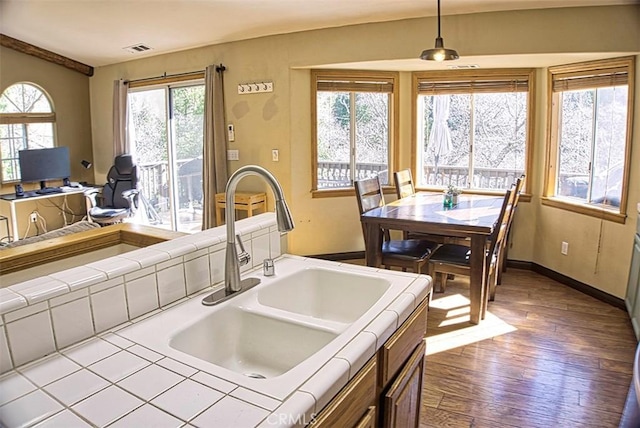 kitchen with a sink, wood finished floors, baseboards, tile countertops, and visible vents