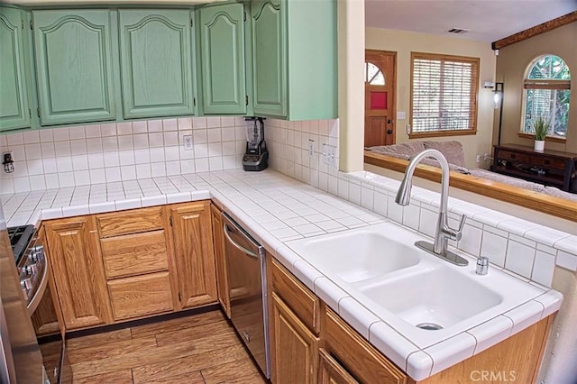 kitchen featuring light wood-style flooring, decorative backsplash, a sink, and stainless steel appliances