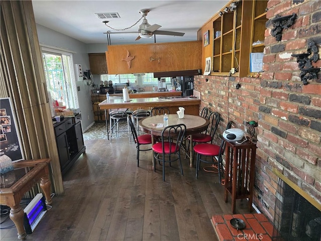 dining room with dark wood-style floors, ceiling fan, visible vents, and a brick fireplace