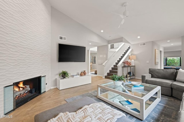 living room featuring stairway, visible vents, a lit fireplace, and ceiling fan