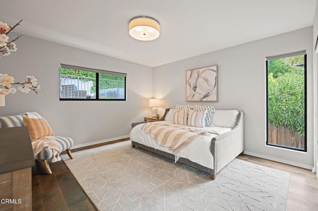 bedroom with multiple windows, baseboards, and wood finished floors