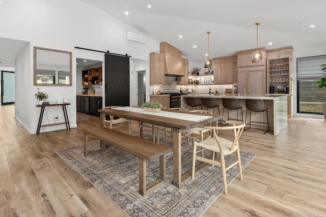 dining space featuring a barn door, light wood-type flooring, recessed lighting, and high vaulted ceiling