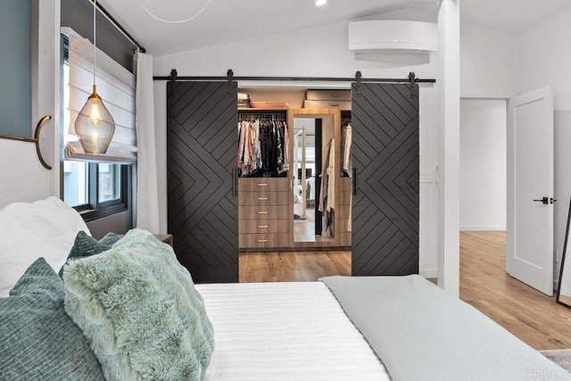 bedroom featuring a barn door, wood finished floors, a walk in closet, and lofted ceiling