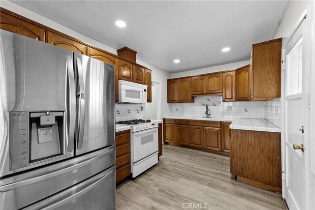 11525 Corby Ave, Norwalk, CA 90650 - kitchen featuring white appliances, brown cabinetry, tasteful backsplash, light wood-type flooring, and recessed lighting
