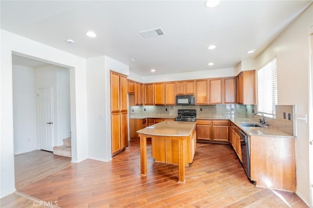 kitchen featuring light wood-style flooring, dishwasher, a sink, black microwave, and gas range oven