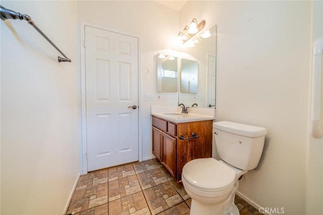 bathroom featuring toilet, vanity, stone finish flooring, and baseboards