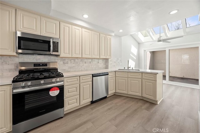 kitchen featuring appliances with stainless steel finishes, a skylight, cream cabinets, and a sink