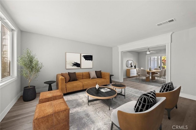 living area with baseboards, wood finished floors, visible vents, and a ceiling fan