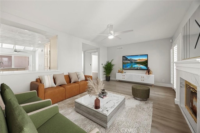 living room featuring a ceiling fan, wood finished floors, visible vents, and a fireplace