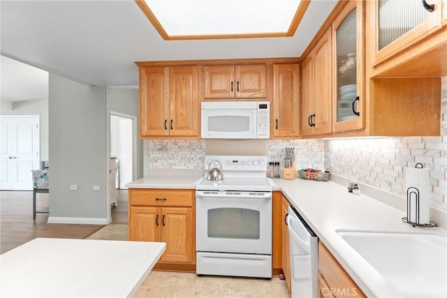 kitchen featuring white appliances, decorative backsplash, light countertops, glass insert cabinets, and baseboards