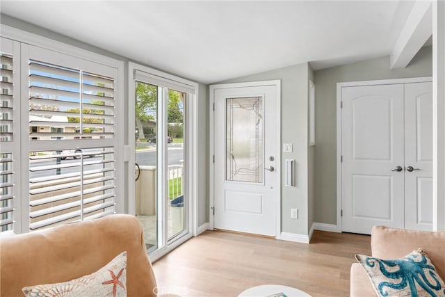 doorway with light wood-style floors, lofted ceiling, and baseboards