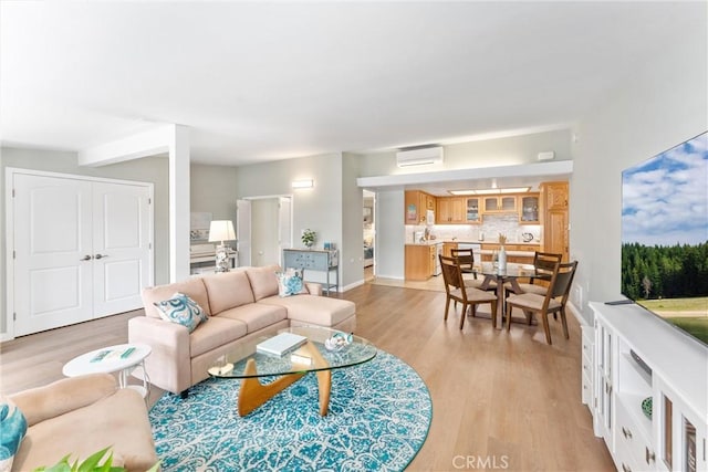 living room with a wall mounted air conditioner, light wood-type flooring, and baseboards