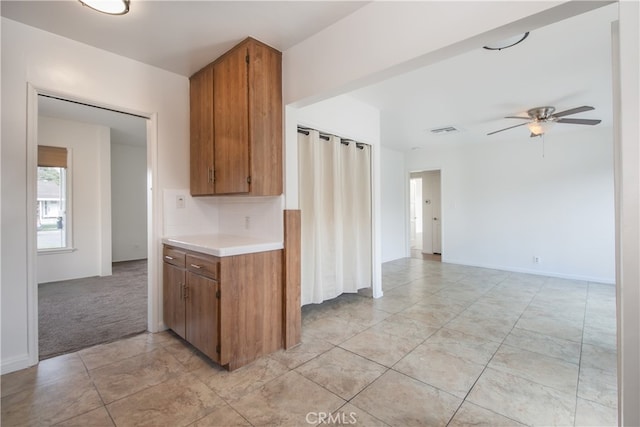 kitchen featuring light countertops, light colored carpet, ceiling fan, visible vents, and brown cabinets