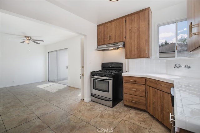 kitchen featuring a sink, under cabinet range hood, gas range, and brown cabinets