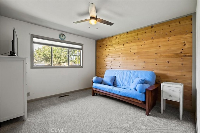 sitting room with wood walls, visible vents, a ceiling fan, baseboards, and carpet flooring