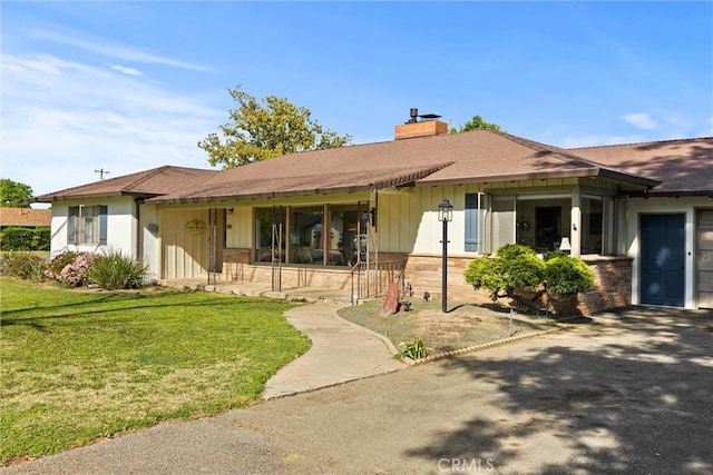 ranch-style home featuring a porch, a chimney, roof with shingles, and a front yard