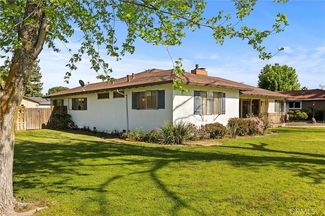 back of house with stucco siding, a lawn, a chimney, and fence